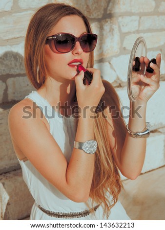 seductive blond woman sitting against a wall and doing make up .