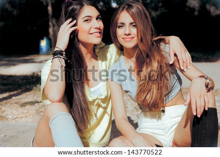 Two Happy, Beautiful Best Friends Sitting In Park On A Summer Day And Smiling. Horizontal Shot. Soft Sunny Colors