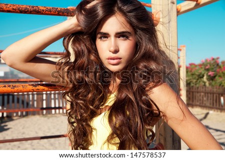 beautiful brunette with long wavy , shine hair and fresh make up posing on a sunny day. Horizontal summer street shot.