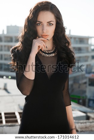 Beautiful woman with long black wavy hair and black outfits. Bright make up face .Sexy look. Street style. Vertical shot.