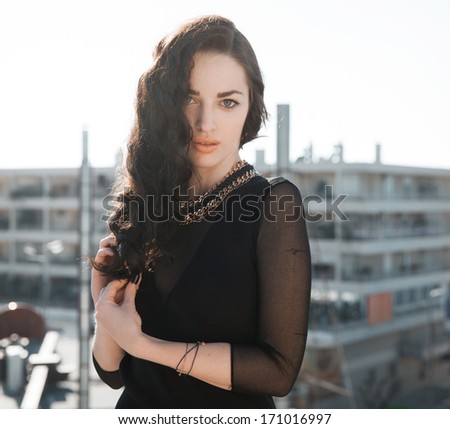 Beautiful brunette woman with long black wavy hair and black outfits. Bright make up face .Sexy look. Street style. Vertical shot.