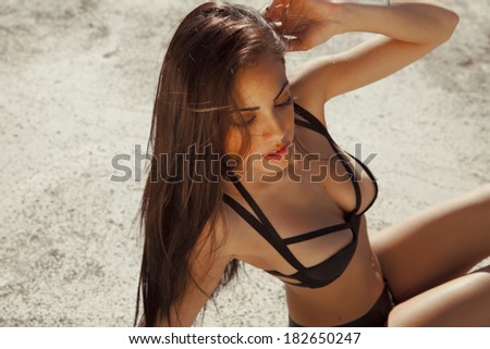 Attractive tanned woman in black bikini posing on hot sunny day. Bronze tan. outdoors shot. Horizontal photography.