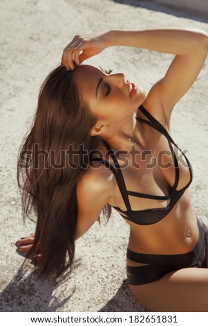Attractive tanned woman in black bikini posing on hot sunny day. Bronze tan. outdoors shot. vertical