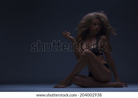 summer woman in glamorous bikini and long curly hair. fool body shot. toned in warm colors. studio shot on a dark blue background. horizontal. copy space for your text