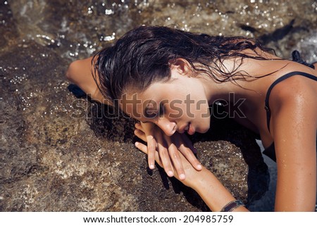 Carefree beautiful brunette with wet look and bright makeup by the sea. Toned in warm colors. horizontal shot, outdoors