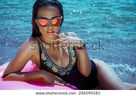 fashion outdoor photo of sexy beautiful woman with long hair in elegant black bikini with accessories relaxing on summer beach. horizontal shot