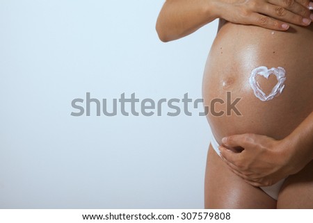 Pregnancy care. Belly of pregnant woman and heart from moisturizing cream for stretch marks. Copy space for your text. studio shot. Horizontal
