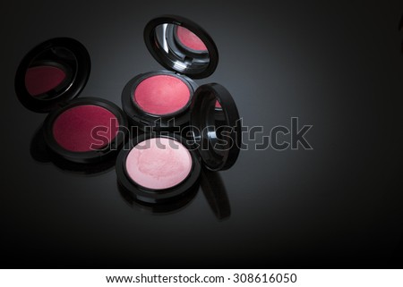 Makeup powder and pink blusher in black case isolated on dark background with reflection. Copy space for your text. Studio shot. Horizontal