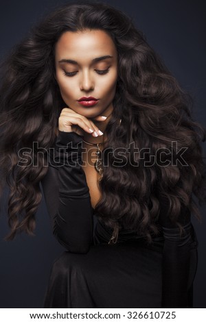 Beautiful young woman with long wavy hair and black elegant dress. Studio shot, Vertical