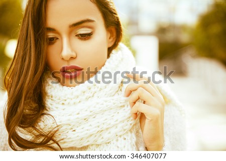 Beautiful  young smiling brunette woman wearing knitted sweater and scarf. Fall and winter fashion concept. Bokeh background. Outdoors shot. Horizontal