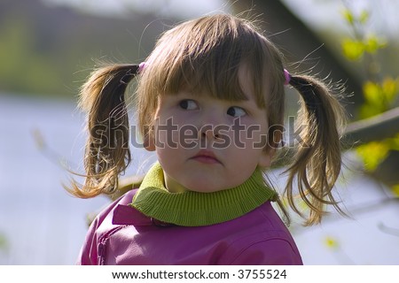 Curious little girl with tails in dressed in pinl coat in the park