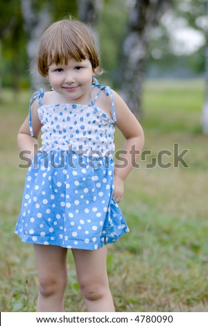 Innocent little girl wearing blue spotted dress with black Devil\'s eyes and smile in the woods