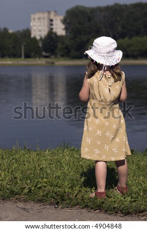 Little girl wearing pretty dress and white hat looking away on the back of a river