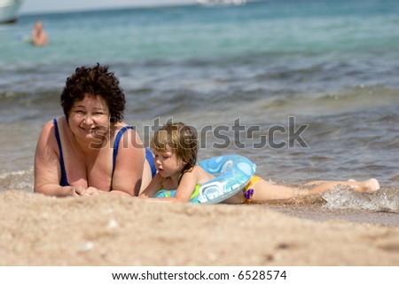 Grandmother and grandchild lying in the water on the beach hot sunny day