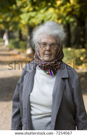 Old lady walking in the autumn park with sad face