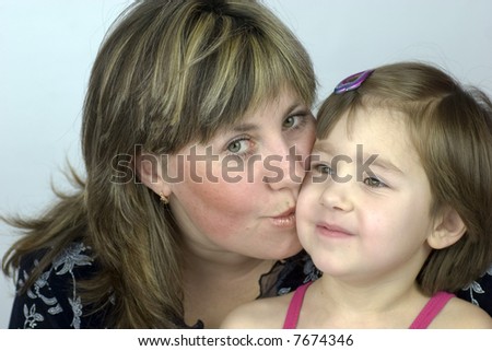 Middle aged mother kissing her little daughter and looking into the camera, both have green eyes