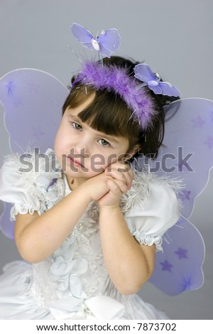 Little girl wearing fairy costume with wings looking at you with sad smile