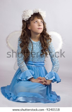 Girl wearing artifical wings beautiful blue dress and white bows for a holiday sitting on a floor looking up