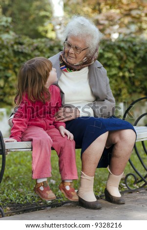 Great grandmother and child sitting on a bench in the park and looking at each other