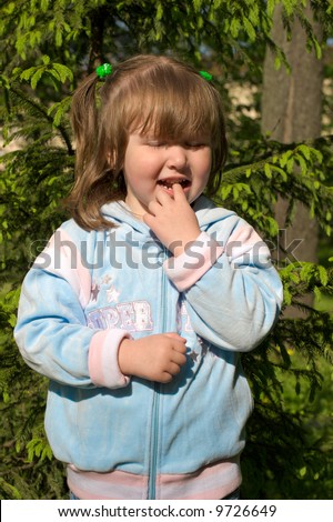 Curious little girl standing near pine tree her eyes are closed because of sunlight