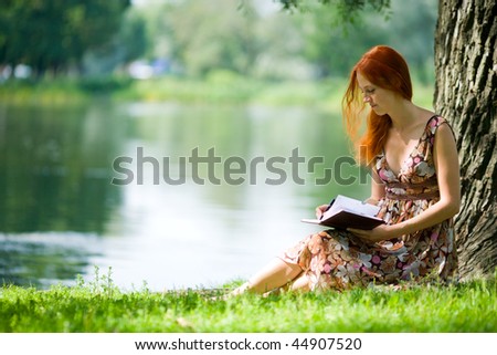 Young redhead woman studying in summer park