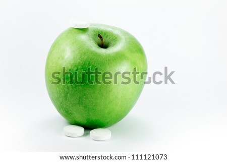 A granny smith apple with a three pills on a white background