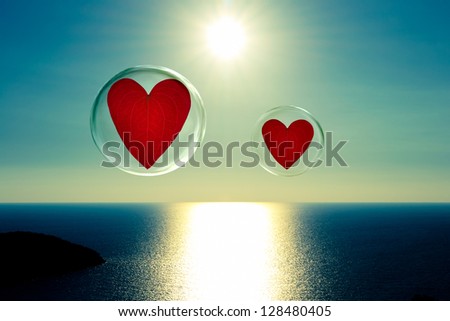 Two hearts in bubbles that float above a sparkling sea with the sun in the background