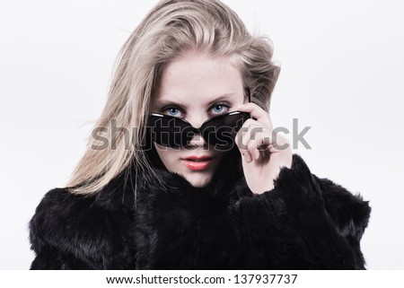 snobbish upper class girl looking out from behind her dark glasses. Wearing a black fur jacket with a white background behind