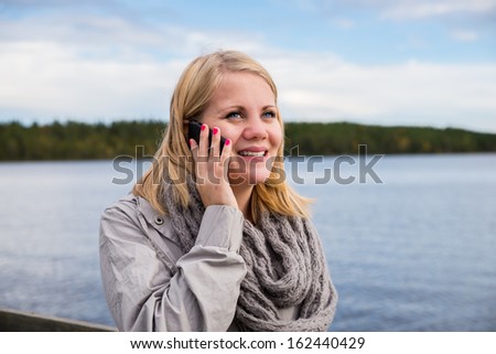 young woman talking on the phone and smiling with lake and sky in the background