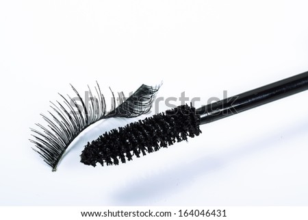 One bent false eyelash and a mascara brush on a white background
