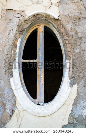ragged oval window in an old building with peeling paint