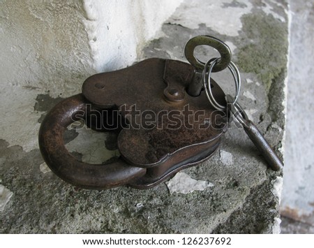 Old, rusty padlock with keys on a metal ring on the gray concrete ledge