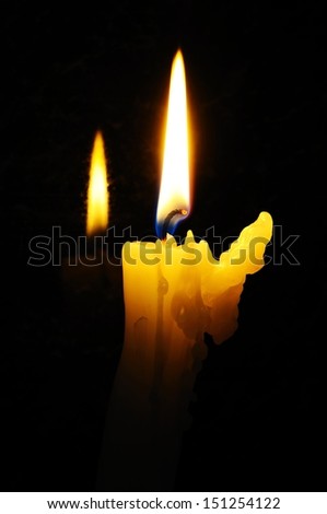 White candle with wax running down side of candle with reflection against a black background.