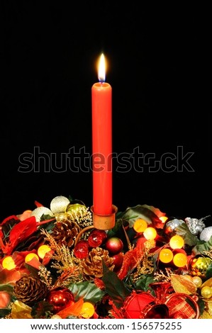 Red candle, Christmas flowers and red berry lights against a black background.