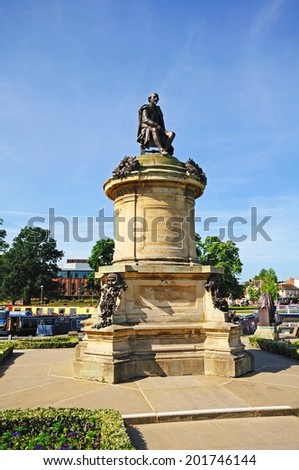 STRATFORD-UPON-AVON - JUNE 12, 2014 - Statue of William Shakespeare sitting on top of the Gower Memorial with the Royal Shakespeare Theatre to the rear, Stratford-upon-Avon, England, UK, June 12, 2014