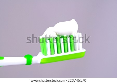 Green and white toothbrush with white toothpaste against a grey background.