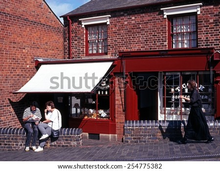DUDLEY, UK - SEPTEMBER 23, 1997 - Couple sitting eating on a wall outside a Victorian shop with a Victorian woman walking along in the Black Country Museum, Dudley, England, UK, September 23, 1997.
