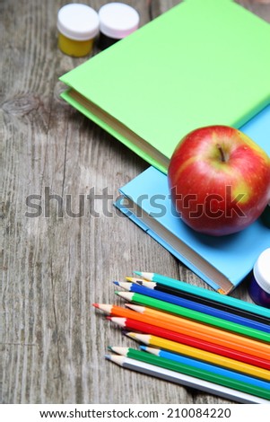 Books, pencils and an apple on a wooden background