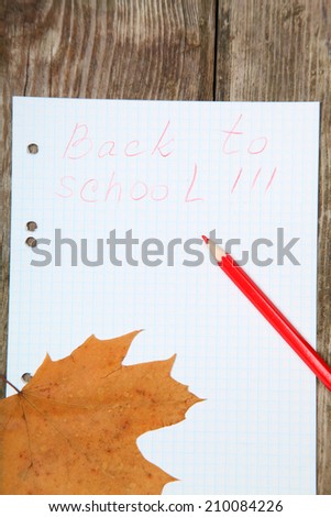 Checkered sheet, maple leaf and pencil on the wooden background