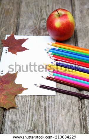 Checkered sheet, maple leaf and pencils on the wooden background