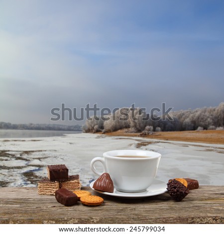 Cup of tea and chocolates on the wooden table, on the background of winter river