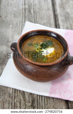 Cabbage soup in a clay pot on old wooden table .