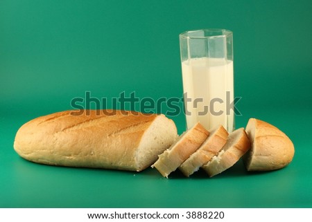 Long loaf and glass of milk on a green background.