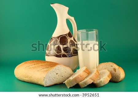 A long loaf, a glass of milk and a jug on a green background.