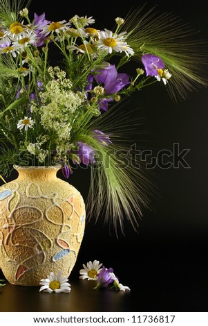 Vase with bouquets of field flowers are photographed on a black background.