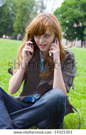 The girl talks by two mobile phones, sitting on a grass