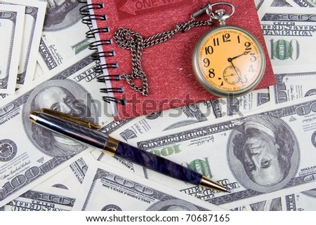 Pocket watch, notebook and pen on a stack of dollars, reflecting time and money