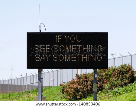A sign near a major airport urges citizens to report suspicious activity.