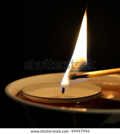 A tea candle in a tea cup being burned with a match