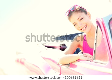 Woman driving vintage retro convertible car in pink. Retro style portrait of young beautiful happy smiling asian woman driver.